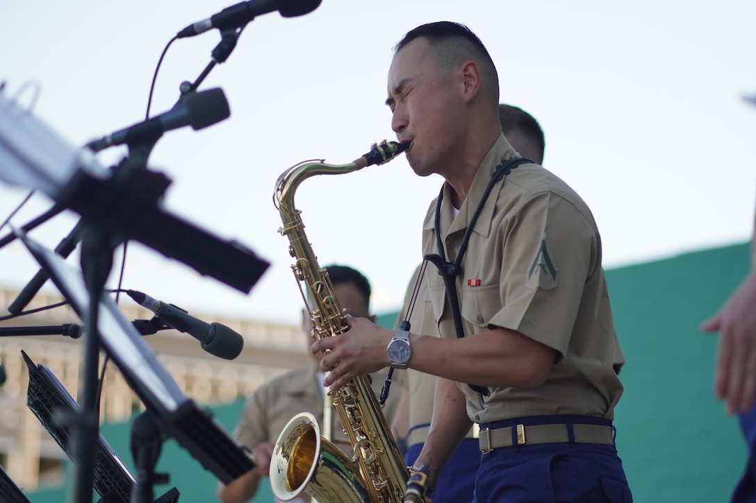 A Marine in dress blues plays saxophone as part of a band.