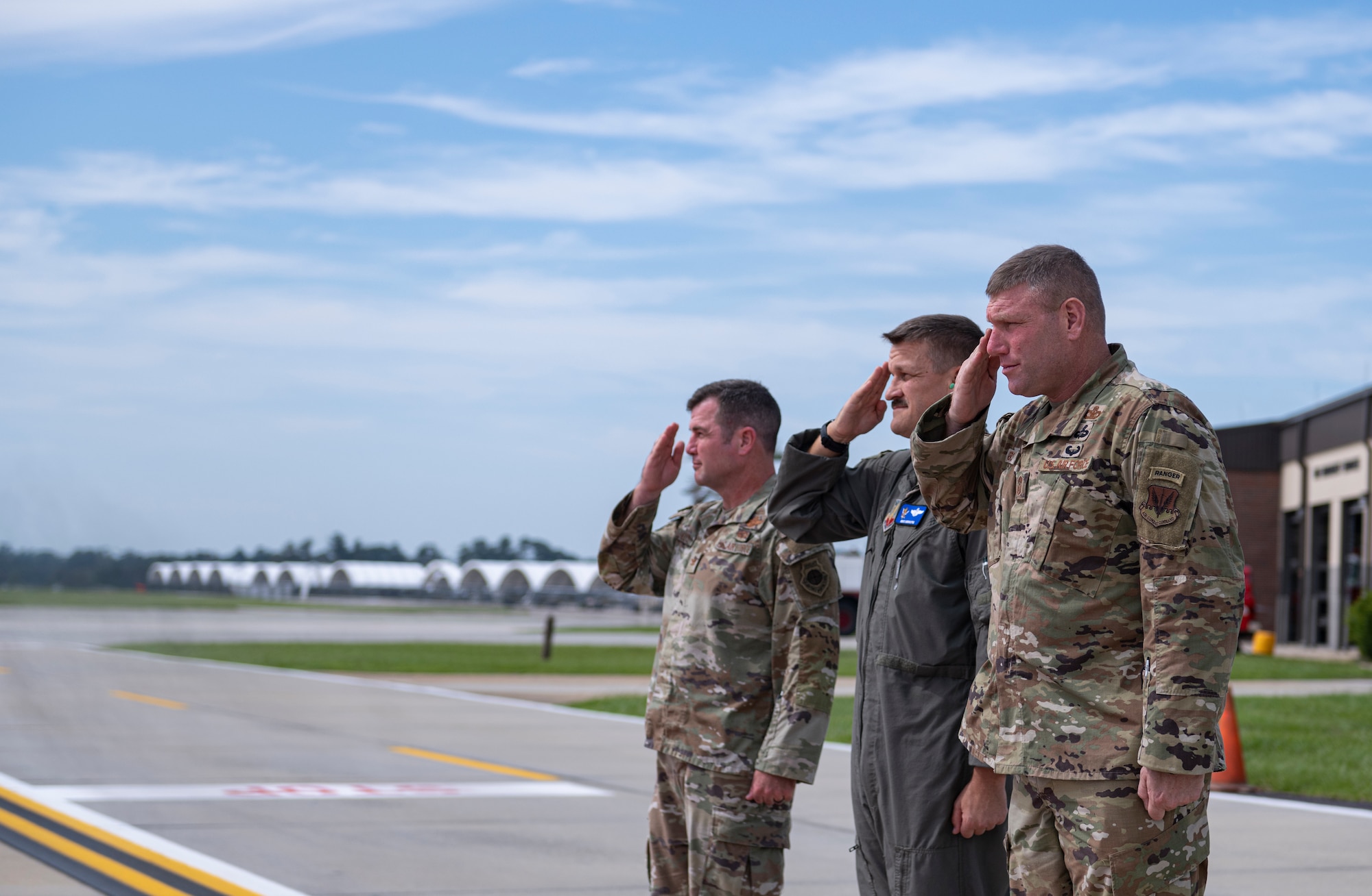 Three Airmen in uniform salute an air craft with a general walking off the plane