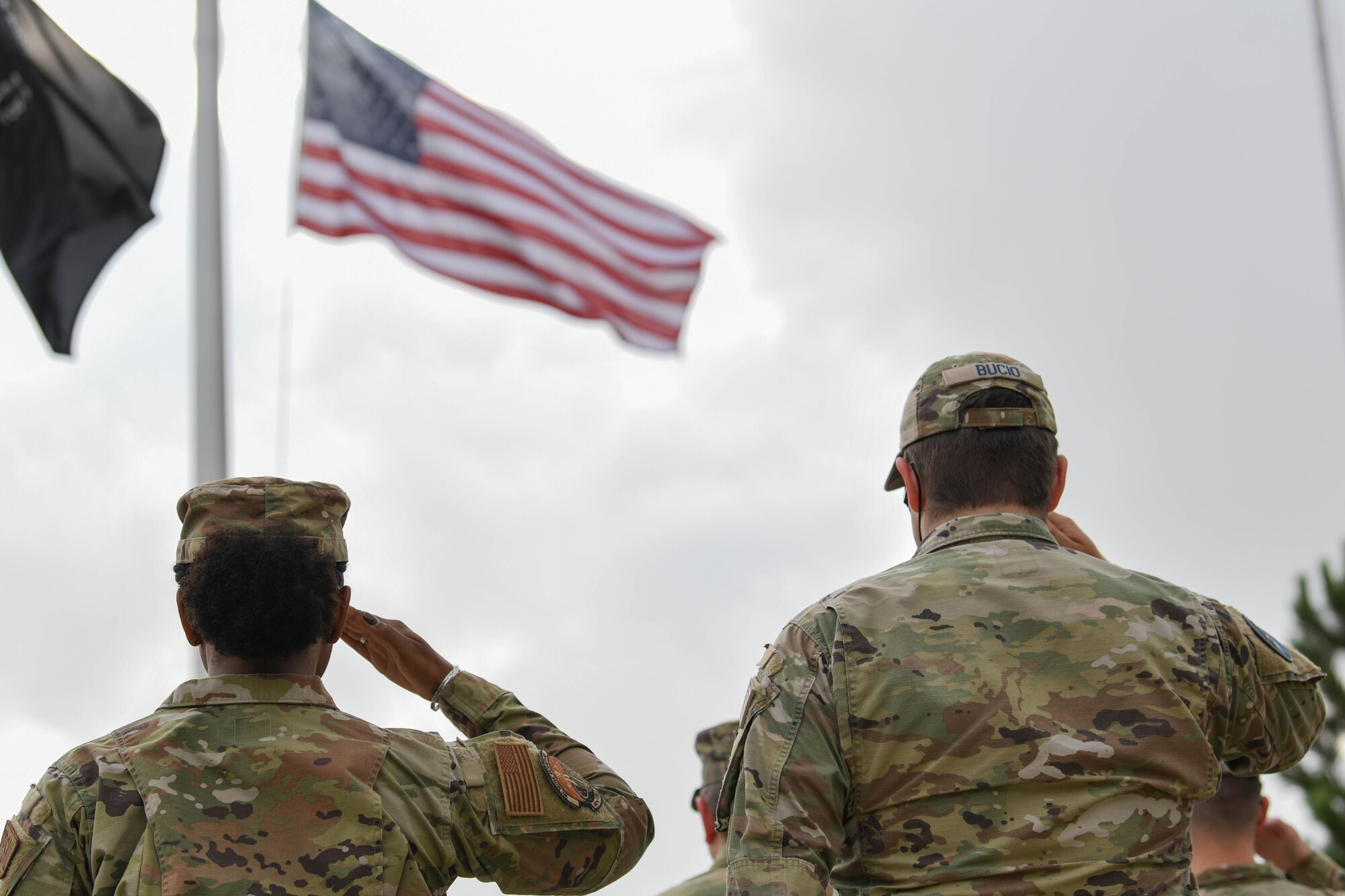 Two military members salute an American flag.