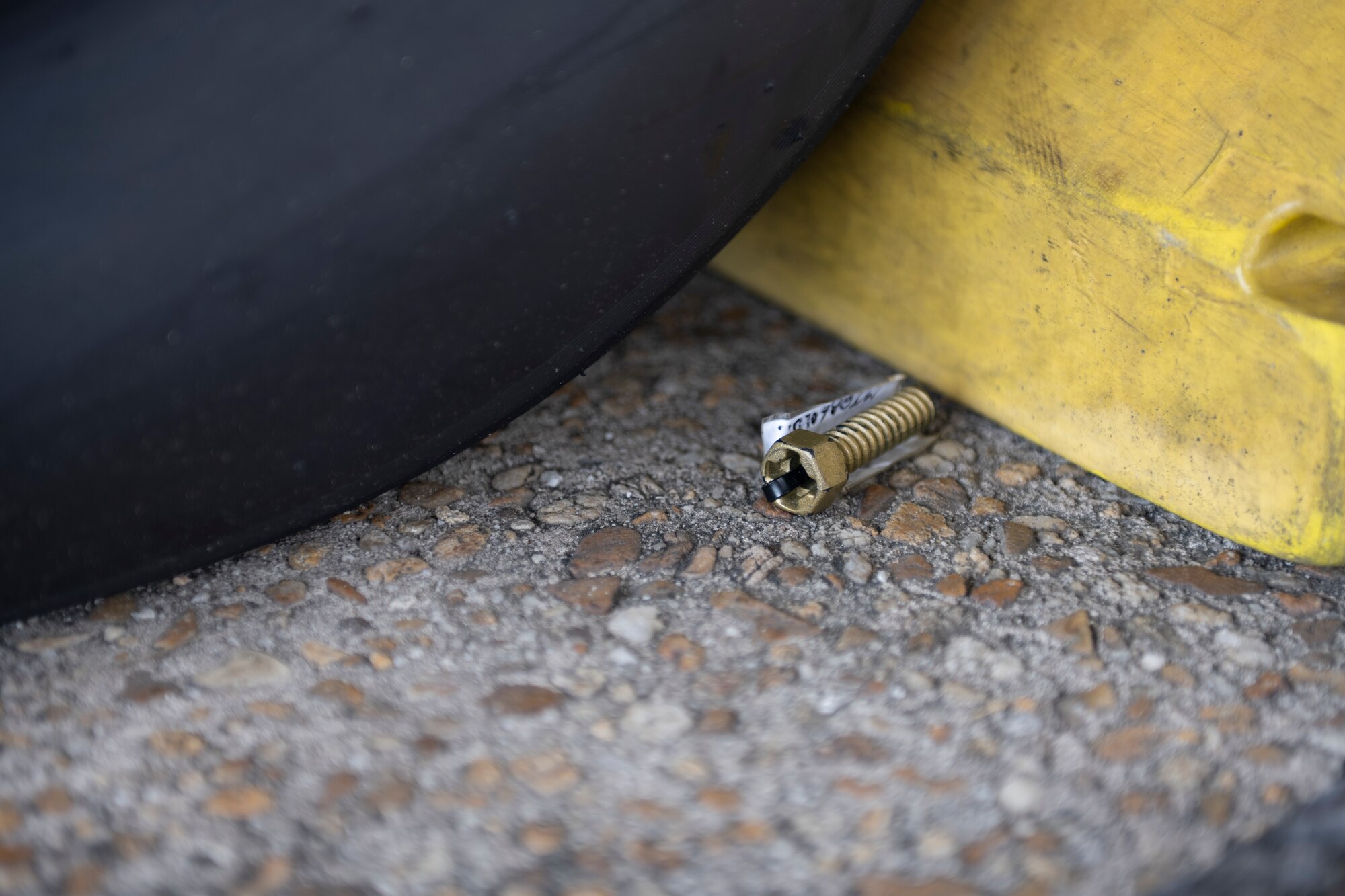 A photo of a bolt painted gold on the ground next to an A-10C Thunderbolt II tire.