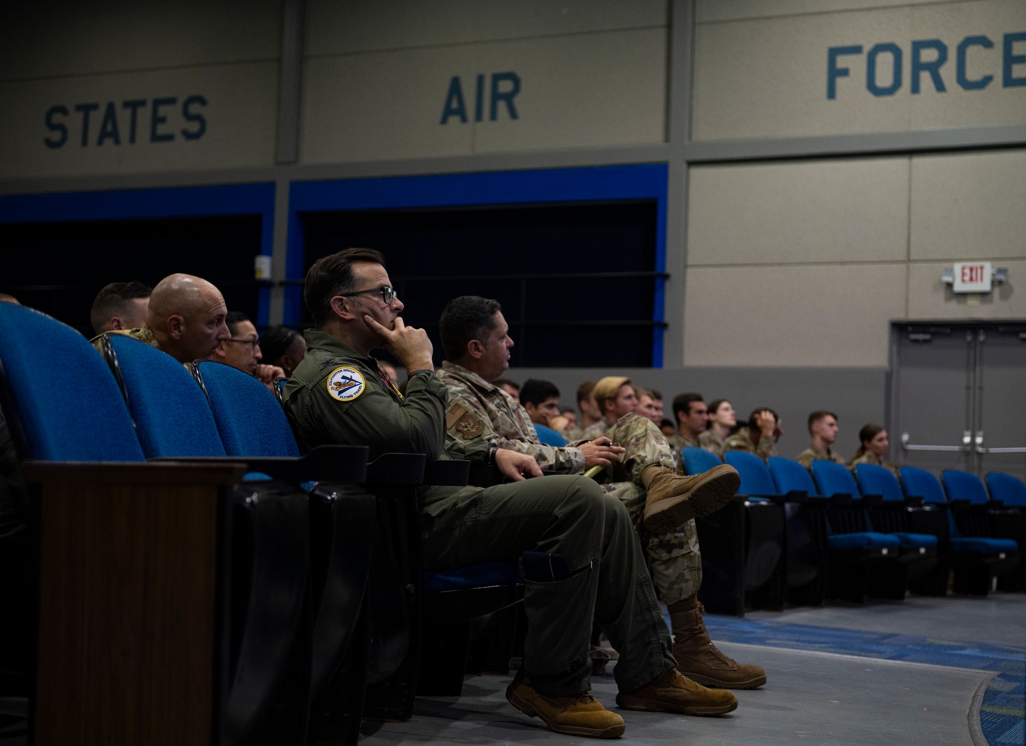 Two commanders sit in the front row listening to the wing commander speak