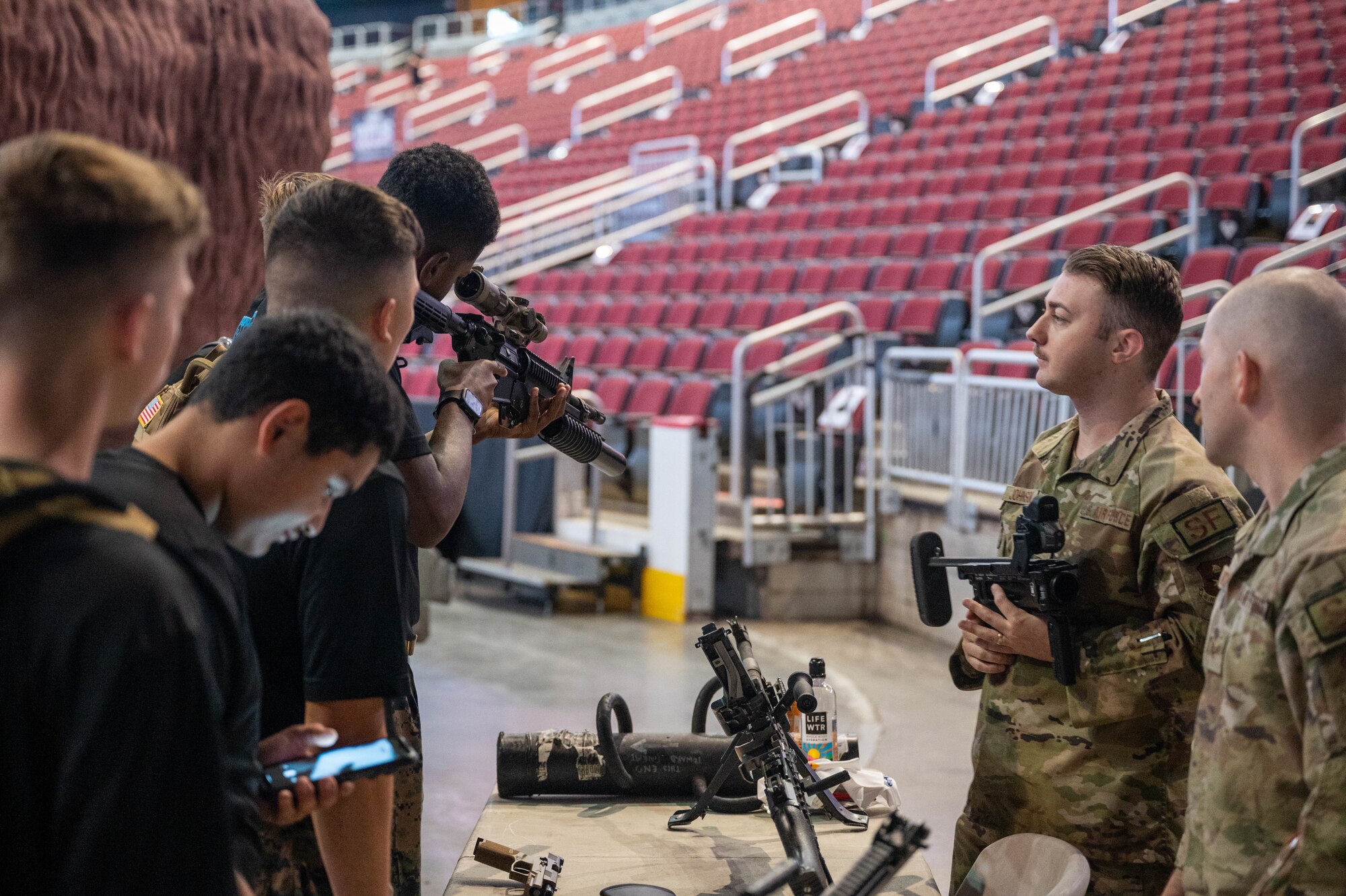 U.S. Air Force Staff Sgt. Austin Johnson, 56th Security Forces Squadron combat arms instructor, and Staff Sgt. Casey Church, 56th SFS armory noncommissioned officer in-charge, showcase various weapon platforms to local Navy Junior ROTC members during the 9/11 Tower Challenge, Sept. 11, 2023, at Desert Diamond Arena, Glendale, Arizona.