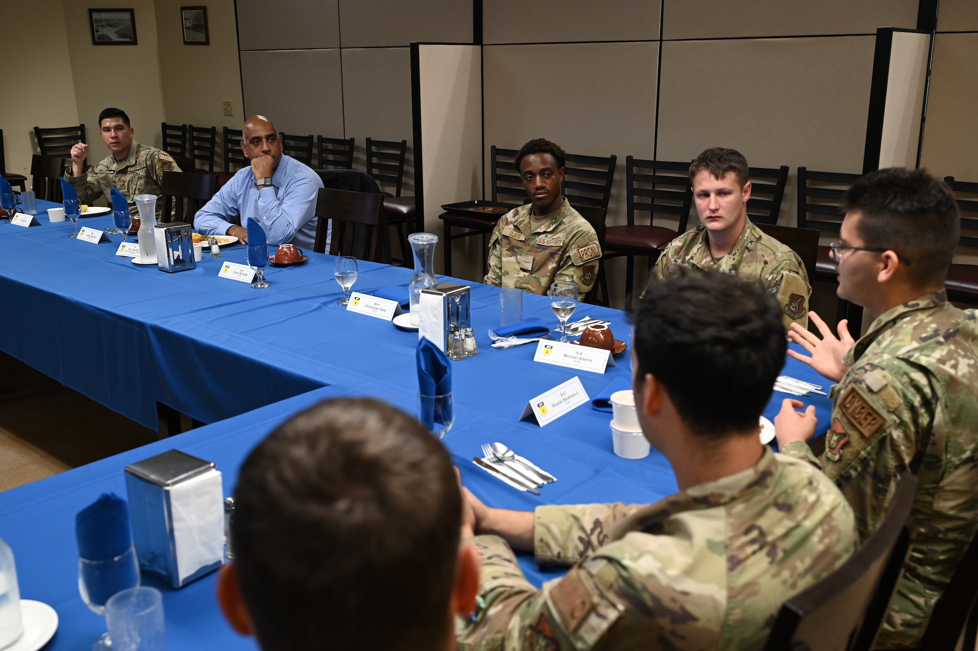 Dr. Ravi Chaudhary sits on a large lunch table with a group of Airmen and listens to their concerns.