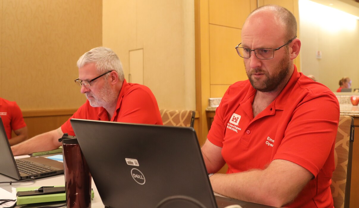 Two men sit at a table working on laptop computers