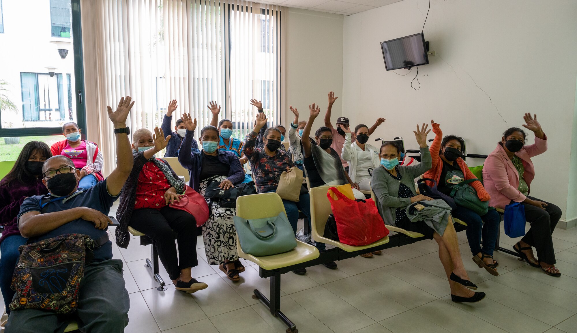 Family members in a waiting room wave to the camera.
