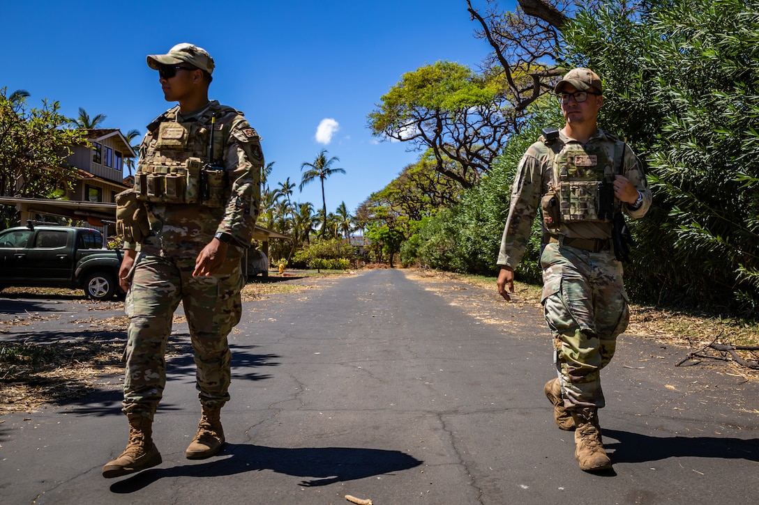 Two airmen wearing tactical gear walk down a road while on security patrol.