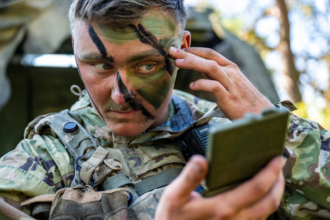 A soldier applies camouflage paint to his face.