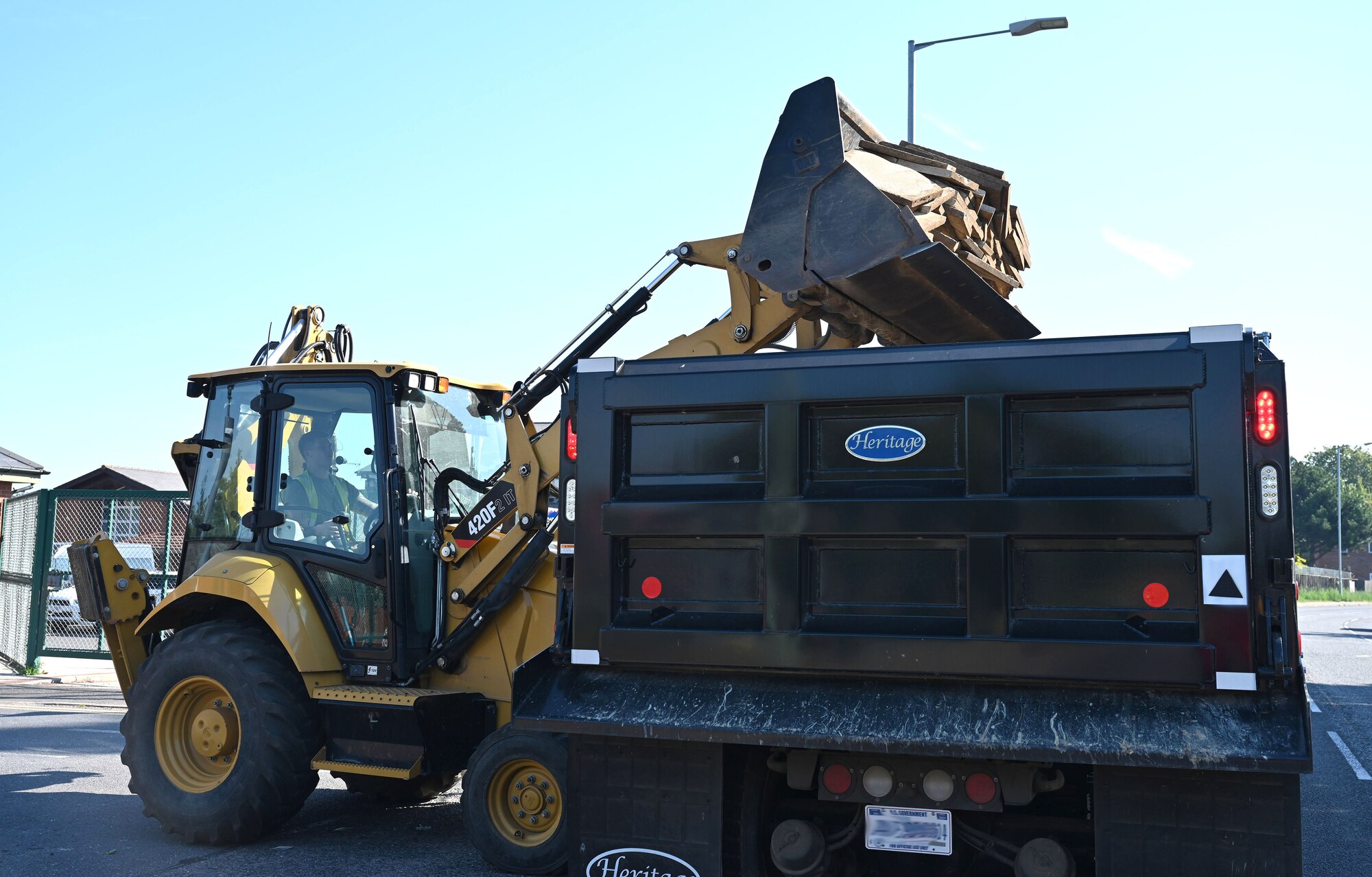 U.S. Air Force Airmen from the 100th Civil Engineer Squadron Heavy Equipment and Pavements shop, otherwise known as “Dirt Boyz,” transfer old paving slabs, weeds and debris from a digger to a truck outside the child development center at Royal Air Force Mildenhall, England, Sept. 7, 2023. The heavy equipment and pavements Airmen, otherwise known as the “Dirt Boyz,” put up new fencing, replaced curbs and pathways, and added a concrete mini hardstand for an additional 100th Security Forces Squadron entry control point to provide easier and safer access for those walking across the main road from base to the CDC gate. (U.S. Air Force photo by Karen Abeyasekere)