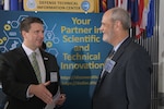 Two men talk in front of a sign that says Your Partner in Scientific and Technical Innovation.