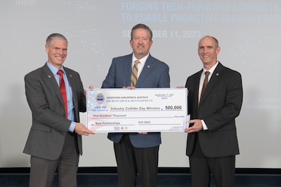 Three men stand on a stage holding a large check