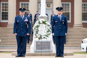 A Air Force member gives speech in uniform next to wreath with white flowers.