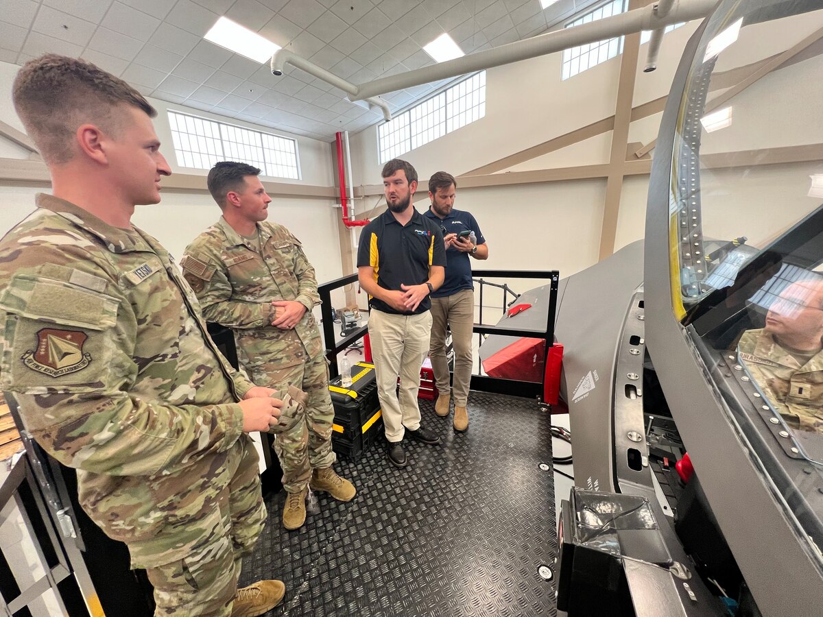 U.S. Air Force Staff Sgt. William Adams, second from left, Detachment 12 egress systems instructor, talks with Junior Force Council, or JFC, members about the F-16 Falcon training model Aug. 8, 2023, as part of the three-day Air Force Research Laboratory, or AFRL, JFC Bluing Trip at Luke Air Force Base, Ariz. Each year, select Air Force bases host junior members of the AFRL workforce to expose members to technologies and people that support the Air Force mission. (U.S. Air Force photo / Kiara Palmer)