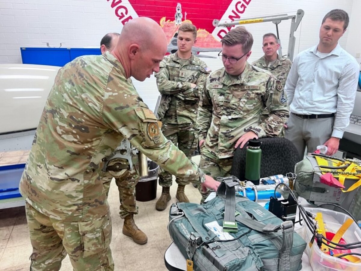 U.S. Air Force Tech. Sgt. Shawn Layou, left, Detachment 12 egress systems instructor, explains to Junior Force Council members, or JFC, the various materials and supplies included in pilot ejection kits Aug. 8, 2023, during a tour of the Field Training Detachment Unit, as part of the three-day Air Force Research Laboratory, or AFRL, JFC Bluing Trip at Luke Air Force Base, Ariz. AFRL JFC Bluing Trips expose junior members of the AFRL workforce to technologies and people that support the Air Force mission. (U.S. Air Force photo / Kiara Palmer)