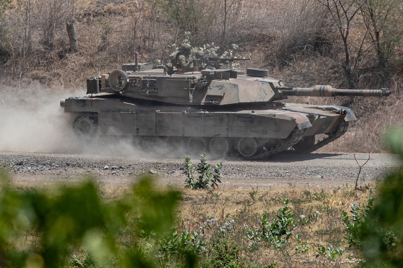A tank patrols on a dusty gravel road.