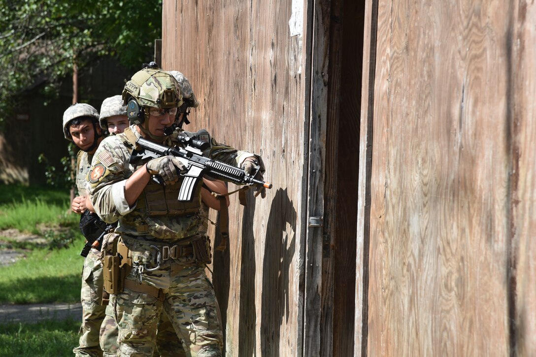 A military member with a practice rifle prepares to enter a building.