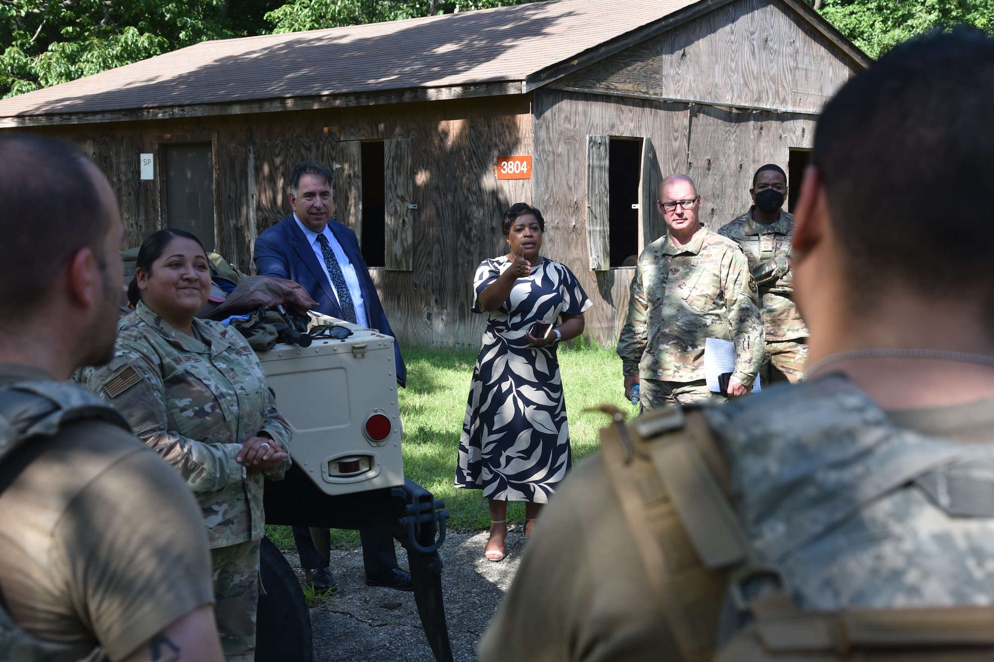 A woman in a dress speaks to people in military uniforms.