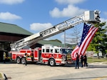Firefighters prepare a flag to raise from a ladder truck.