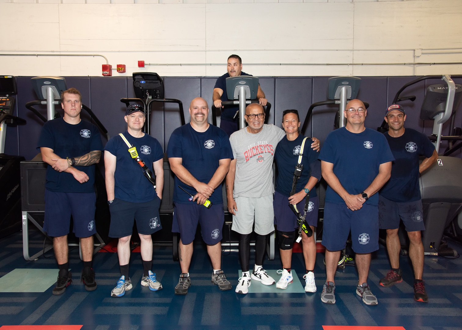 Five people stand in front of stair machines. One person on a machine behind them.