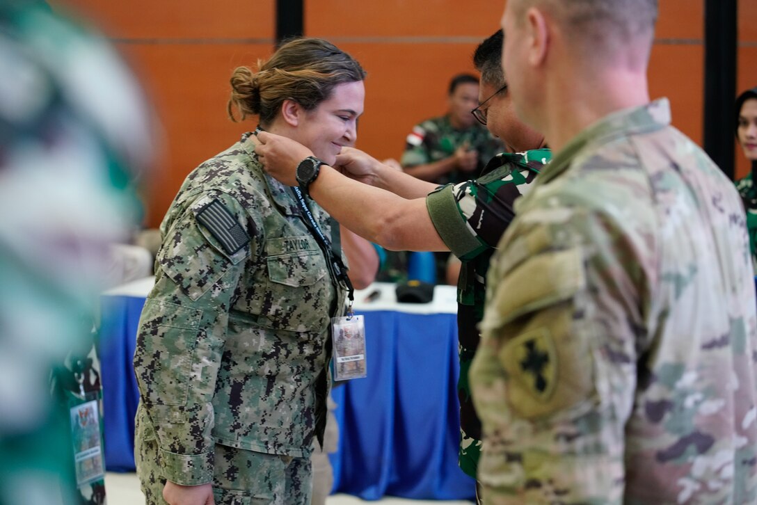 Lt. Abbey Taylor, U.S. Navy, HSC-3, receives the “first badge” from ADM Edi, Commander Guspurla Koormada 2, Tentara Nasional Indonesia (TNI), during the opening ceremony of the staff exercise portion of Super Garuda Shield 2023 (SGS23) August 31, 2023, Surabaya Indonesia. #SuperGarudaShield 2023 is an annual exercise that has significantly grown in scope and size since 2009. #SGS2023 is the second consecutive time this exercise has grown into a combined and #joint event, highlighting the 6 participating and 12 observing nations’ commitment to #partnership and a #freeandopenindopacific. (US Air National Guard Photo by Air Force Master Sgt. Andrew Lee Jackson)