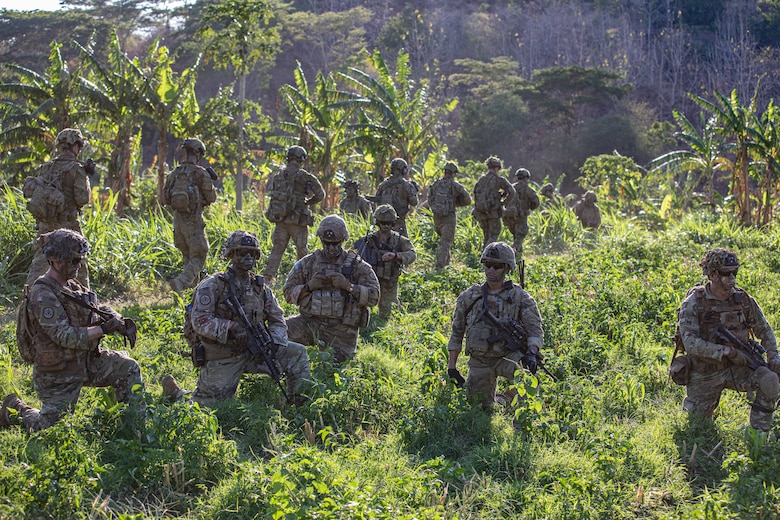 Soldiers patrol in dense foliage.