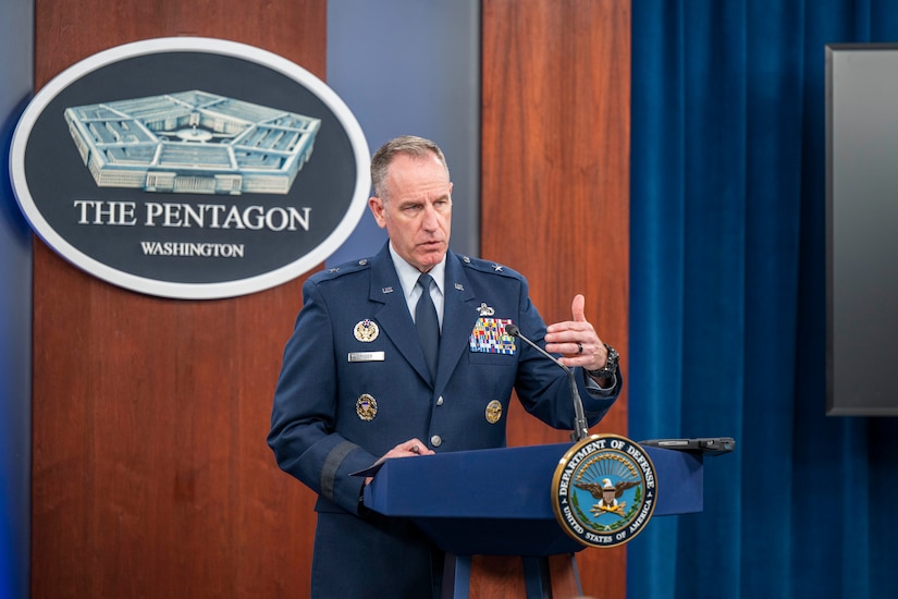 A man in uniform motions with his hand from behind a lectern