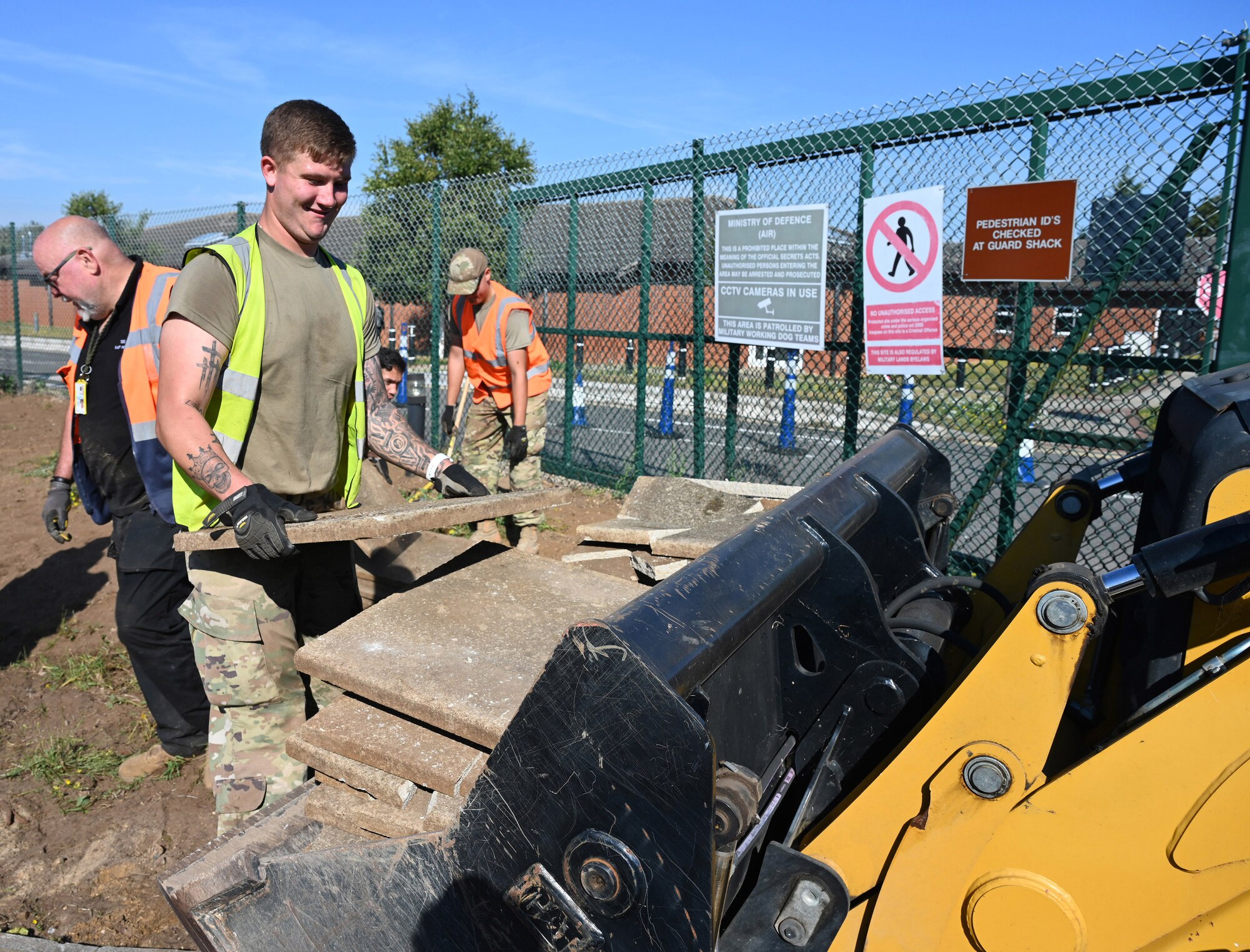Paul Waites, left, 100th Civil Engineer Squadron Heavy Equipment and Pavements foreman, Senior Airman Jordan Weir, center, 100th CES Heavy Equipment journeyman, and Airman Hugo Rodriguez, 100th CES Heavy Equipment craftsman, place old paving slabs into the bucket of a digger ready for disposal outside the child development center at Royal Air Force Mildenhall, England, Sept. 7, 2023. The heavy equipment and pavements Airmen, otherwise known as the “Dirt Boyz,” put up new fencing, replaced curbs and pathways, and added a concrete mini hardstand for an additional 100th Security Forces Squadron entry control point to provide easier and safer access for those walking across the main road from base to the CDC gate. (U.S. Air Force photo by Karen Abeyasekere)
