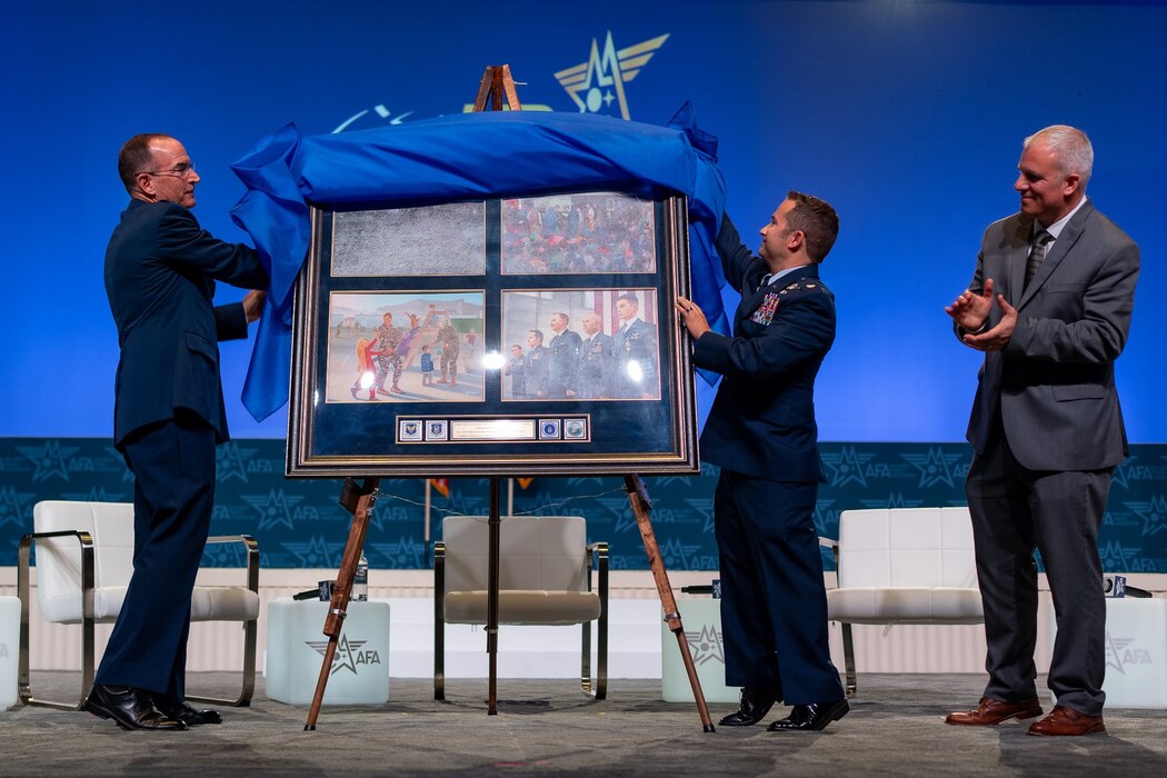 Two people unveil the 75th anniversary painting on stage while another person watches.