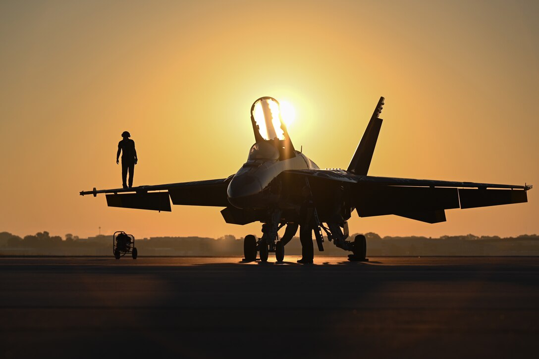 Service members stand on the wing and underneath a jet at twilight.