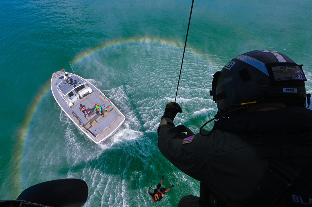 A Coast Guardsman uses a cable to hoist a swimmer from the water to an aircraft.