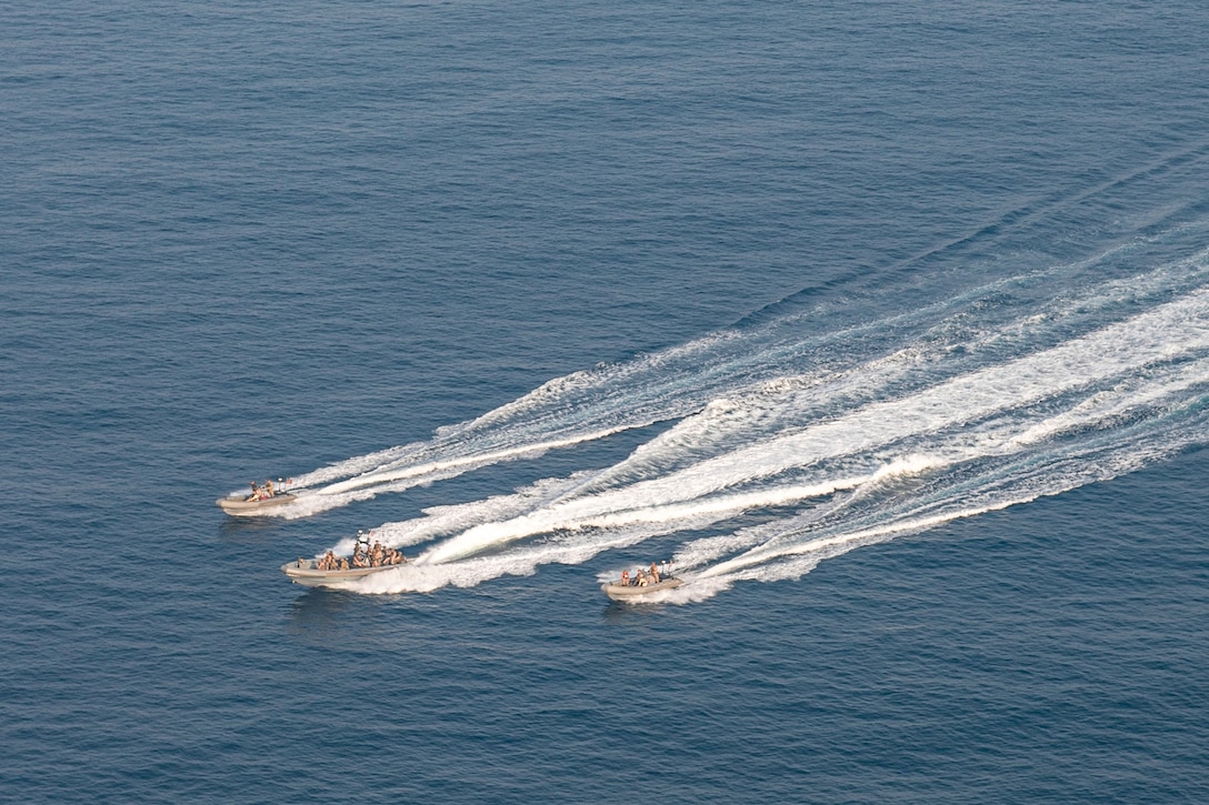 Three inflatable boats sail in open water, creating a wake behind them.