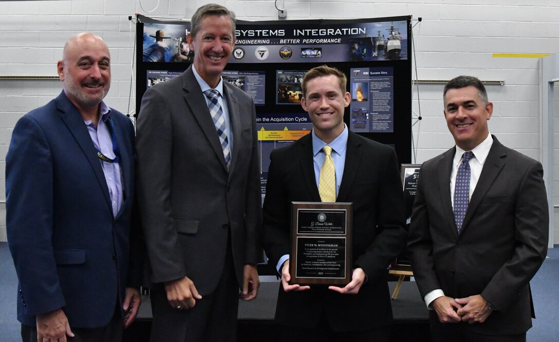 IMAGE: Stephen Cricchi, SES, Executive Director of Naval Air Warfare Center Aircraft Division (NAWCAD), Deputy Assistant Secretary of the Navy Dr. Brett Seidle, SES, and Naval Surface Warfare Center Dahlgren Division (NSWCDD) Technical Director Dale Sisson Jr., SES, stand with Tyler Winningham (third from left) of NAWCAD after he received the G. Dennis White Early Career Human Systems Integration Practitioner Award Sept. 5 at NSWCDD.