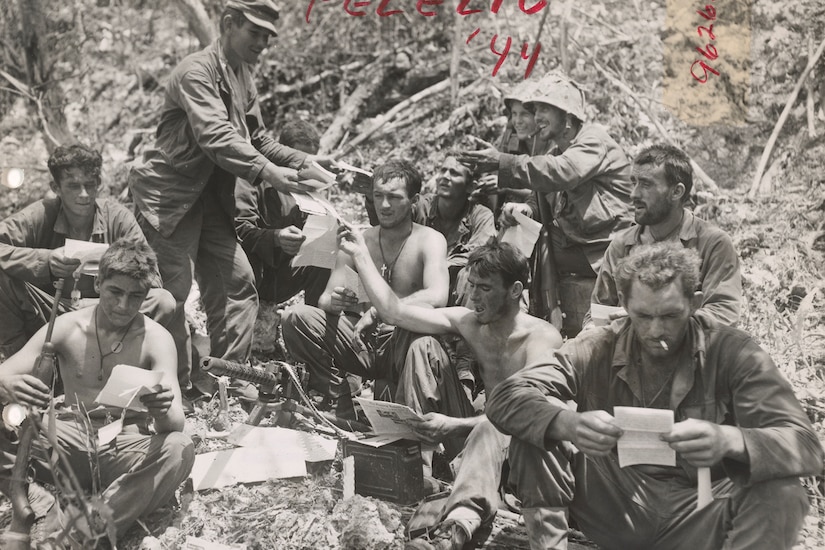 Several people sitting on the ground read letters.