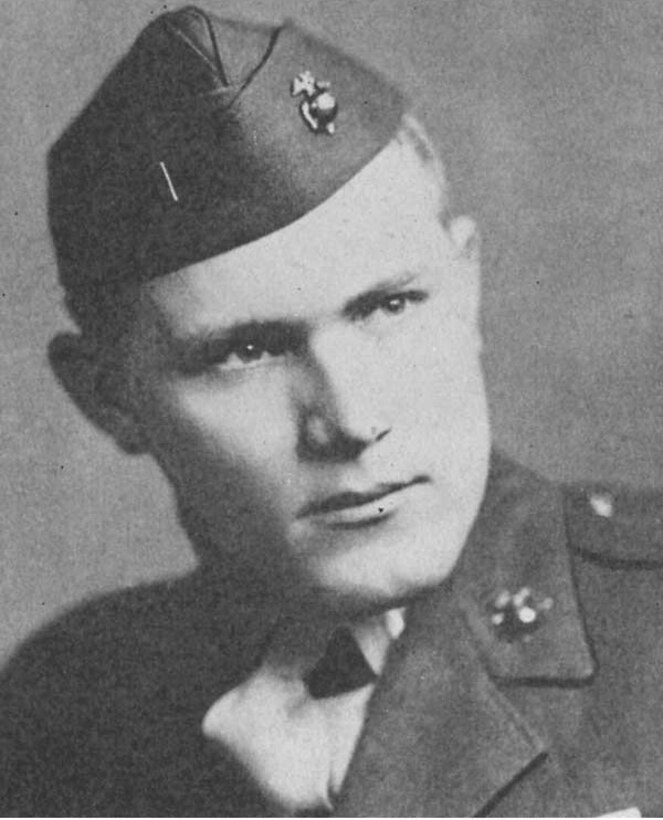 A service member in uniform and cap poses for a photo.