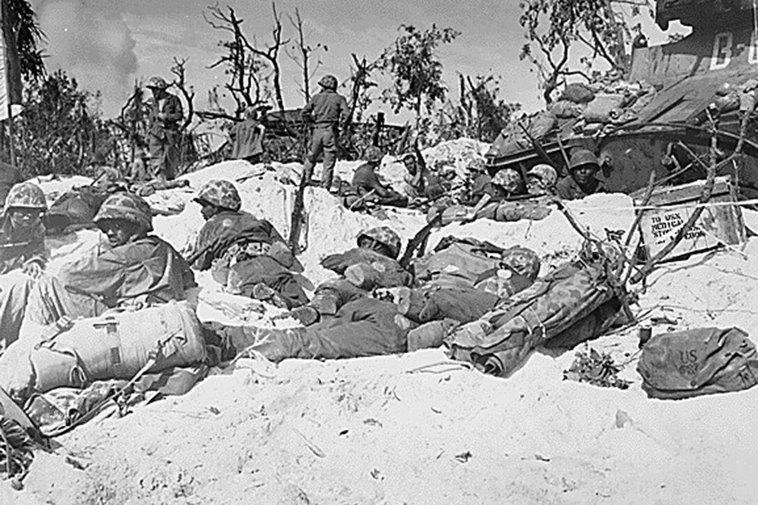Several uniformed service members lie or sit on a beachhead.