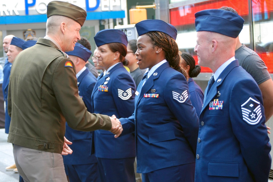 The National Guard Bureau chief shakes hands with a guardsman standing in formation with fellow service members in front of red and white lights.