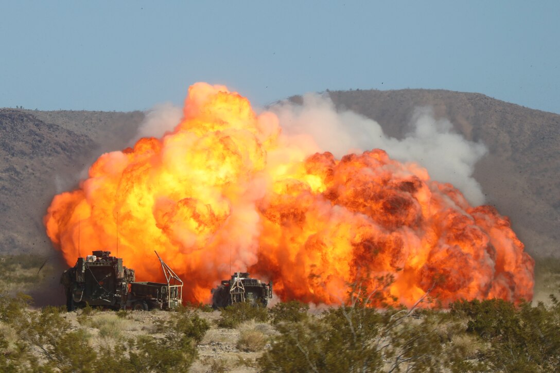 An explosion arises in front of two fighter vehicles in a desert-like area.