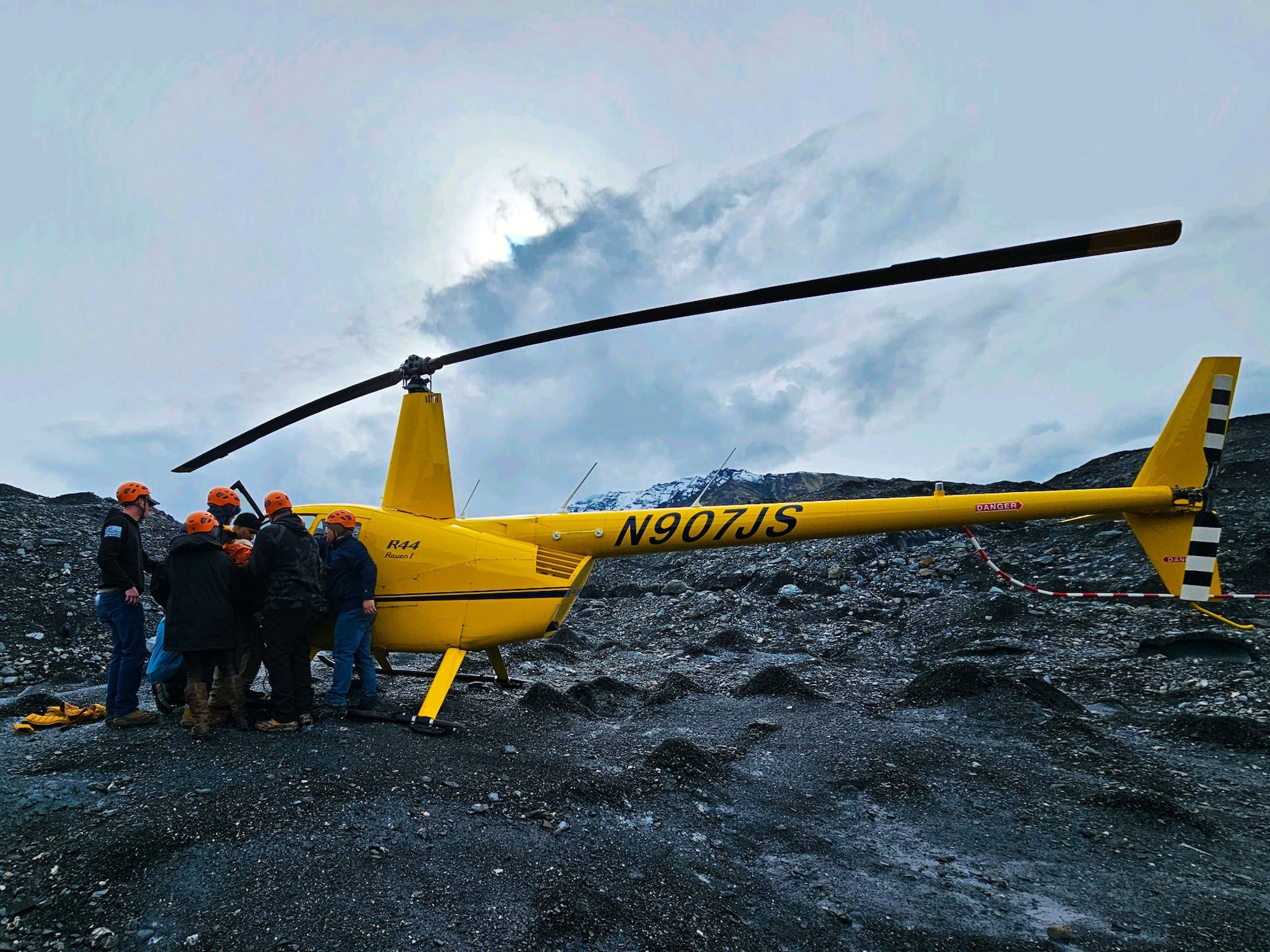 people load stretcher with hiker into a bright yellow helicopter on top of a glacier