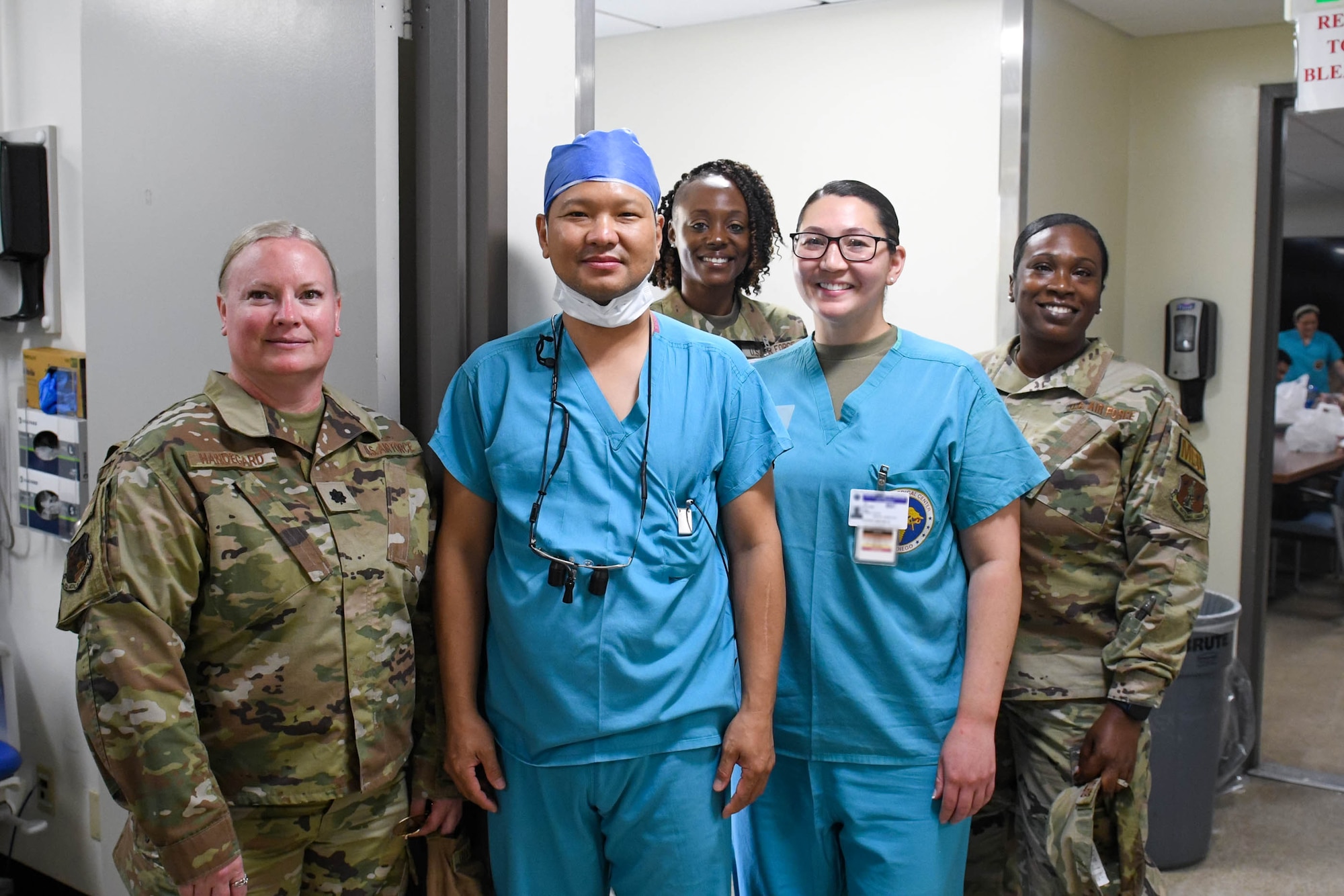 Five members pose for photo, three in OCPs and two in blue scrubs.