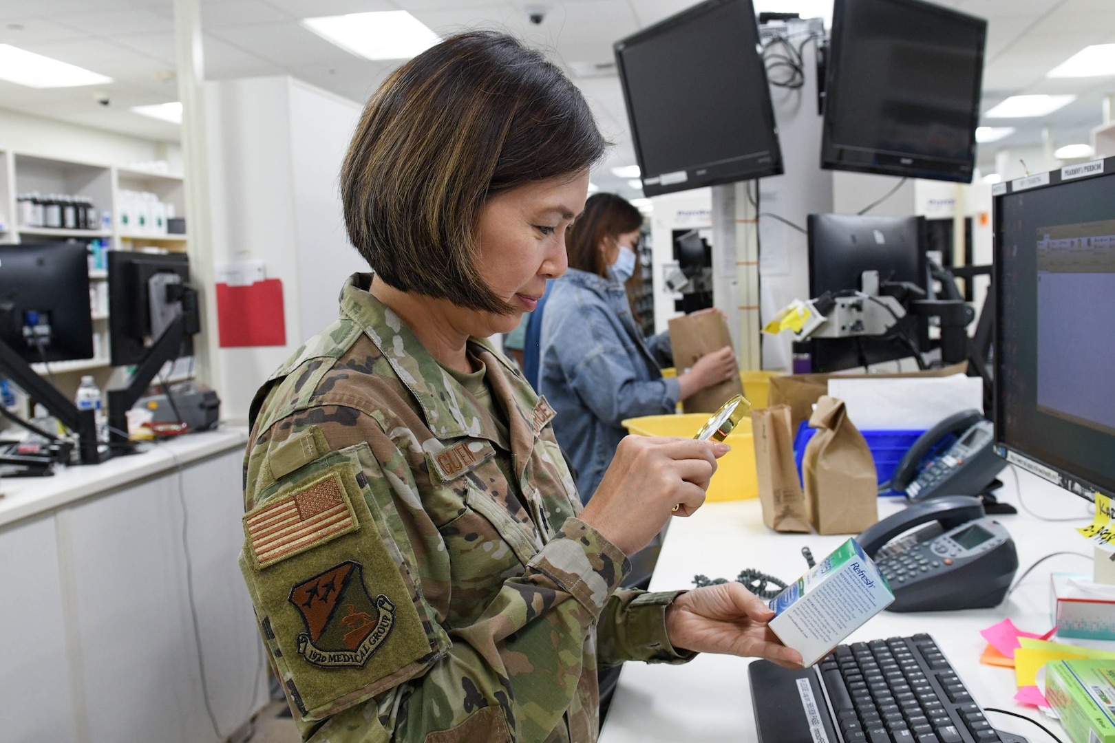 Maj. Nhon Nguyen using magnifying glass to view prescription box.