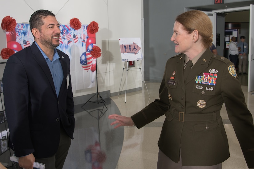 A female uniformed service member speaks to a man, wearing business attire, inside of a building.