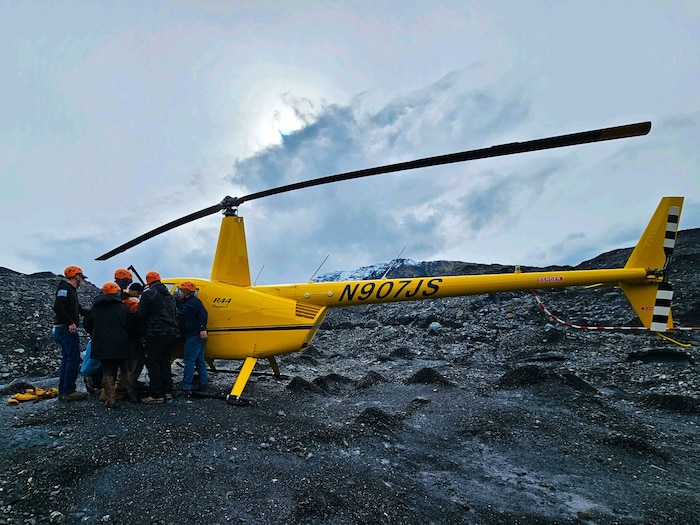 people load stretcher with hiker into a bright yellow helicopter on top of a glacier