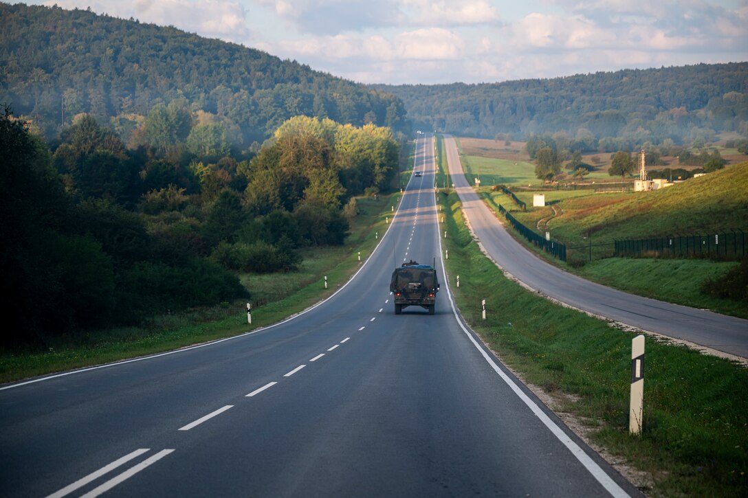 Army soldiers and NATO troops drive down a road in a military vehicle.