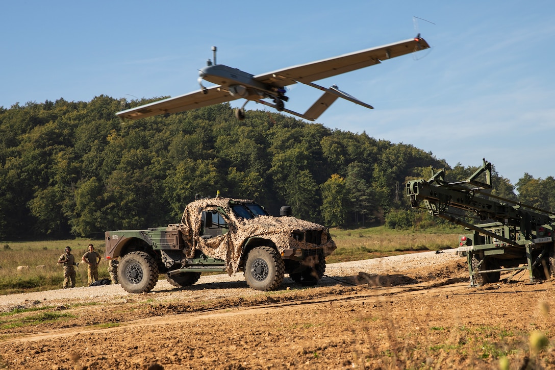 Soldiers watch a launched unmanned aerial vehicle fly overhead.