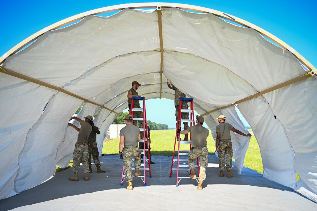 Airmen set up a large tent in a field.