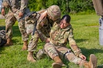 Connecticut Army National Guard Spc. Ashley Hornung, left, a combat medic specialist assigned to the 141st Medical Company (Ground Ambulance), helps Connecticut Army National Guard Spc. Dyamanni Vasquez, right, military police assigned to the 143rd Regional Support Group, stand up during a mass casualty exercise at Fort Drum, New York, Aug. 13, 2023.