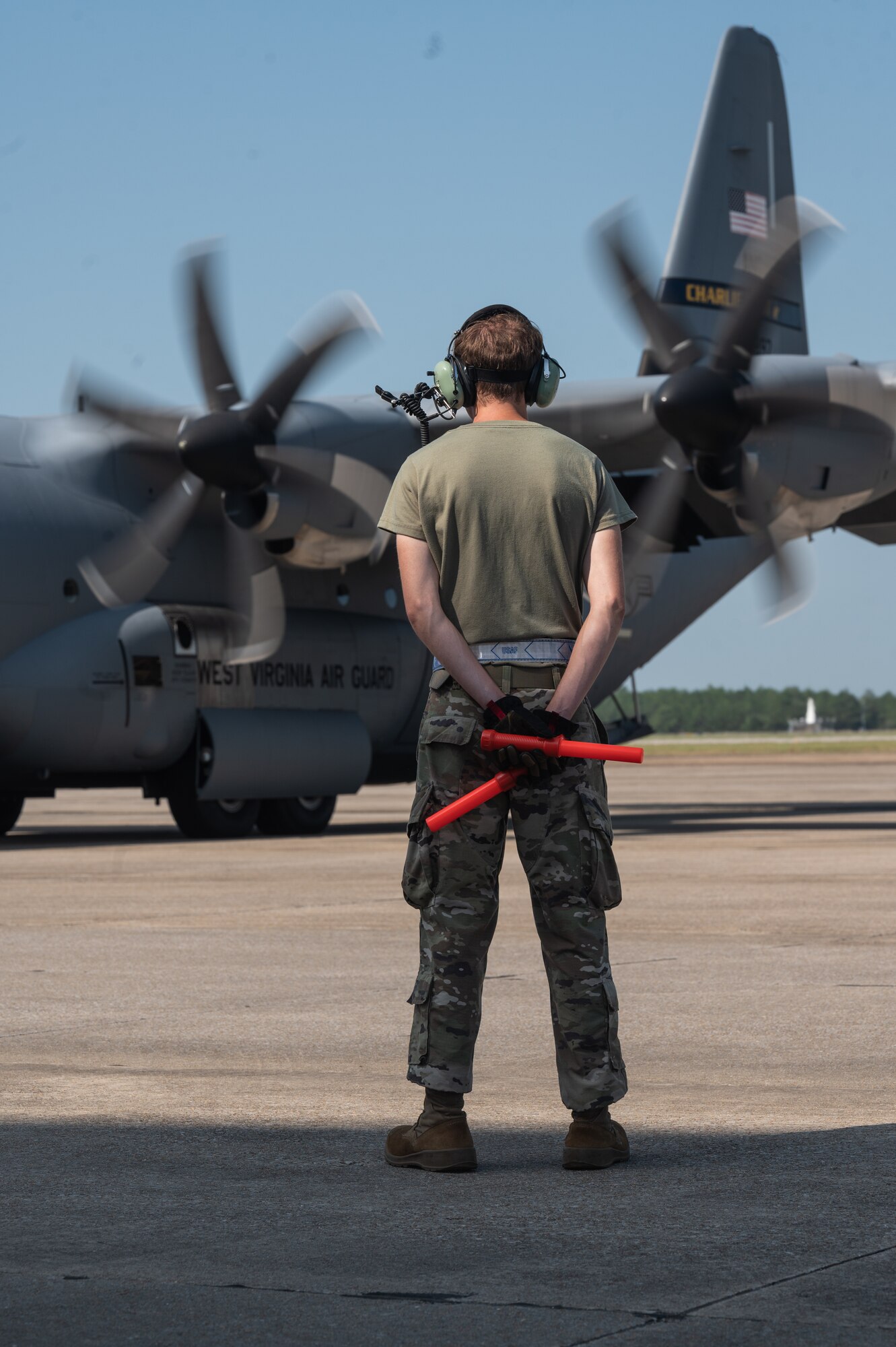 An airman assigned to the 130th Airlift Wing awaits the takeoff of a C-130J-30 during the Fly Away Readiness Exercise (FLARE-V), Sept. 8, 2023, held at Gulfport Combat Readiness Training Center (CRTC), Gulfport, Miss. The fly away readiness exercise is a part of the Air Forces larger mechanism of continuous assessment by the wing, the MAJCOM, and the service through a series of evaluative events including scalable wing-level exercises, joint exercises, complex and operationally informed training events, real-world deployments, and the validation of readiness reporting procedures. (U.S. Air National Guard photo by 2nd Lt. De-Juan Haley)