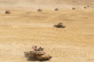 Military tanks maneuver across desert terrain.