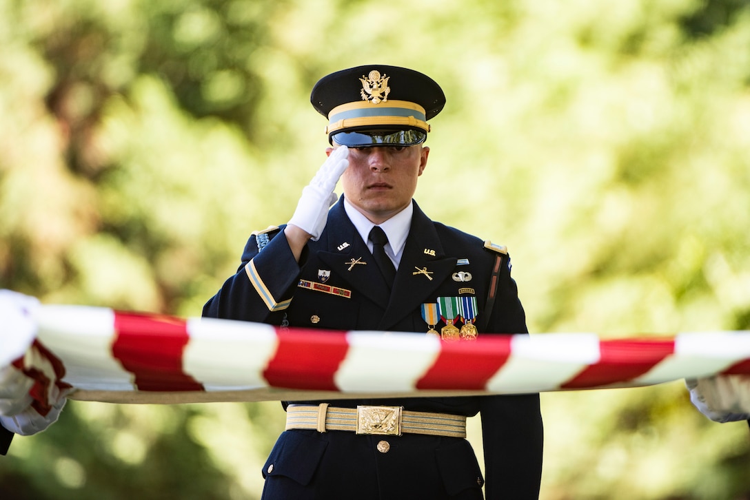 A uniformed soldier salutes as an American flag is folded.