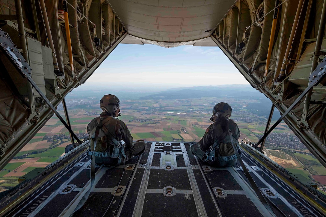Two airmen sit on the ramp of an airborne aircraft.