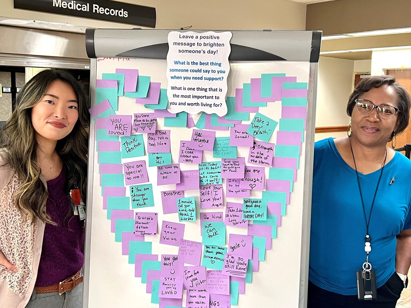 Two women flanking a whiteboard with a flower design created with sticky notes.